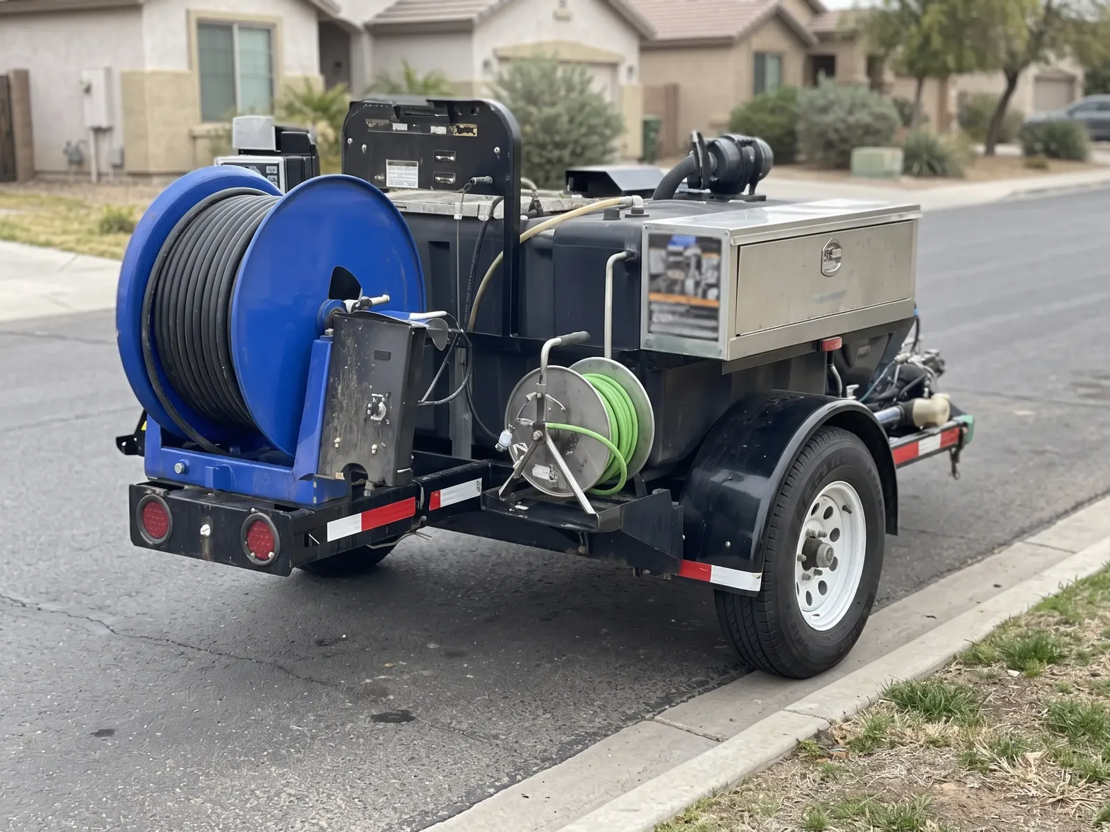 A hose-reel jetting trailer parked at the curb of a residential street