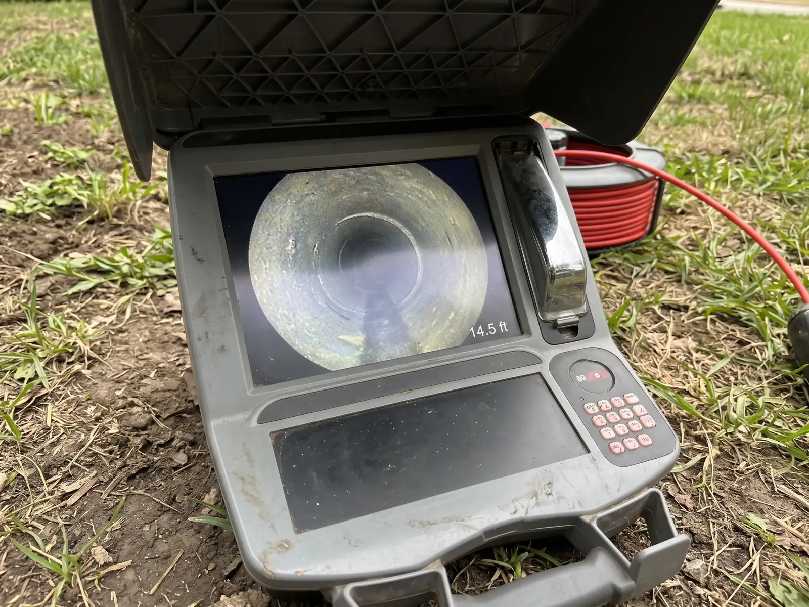 An open sewer camera monitor on the grass, showing the inside of a pipe