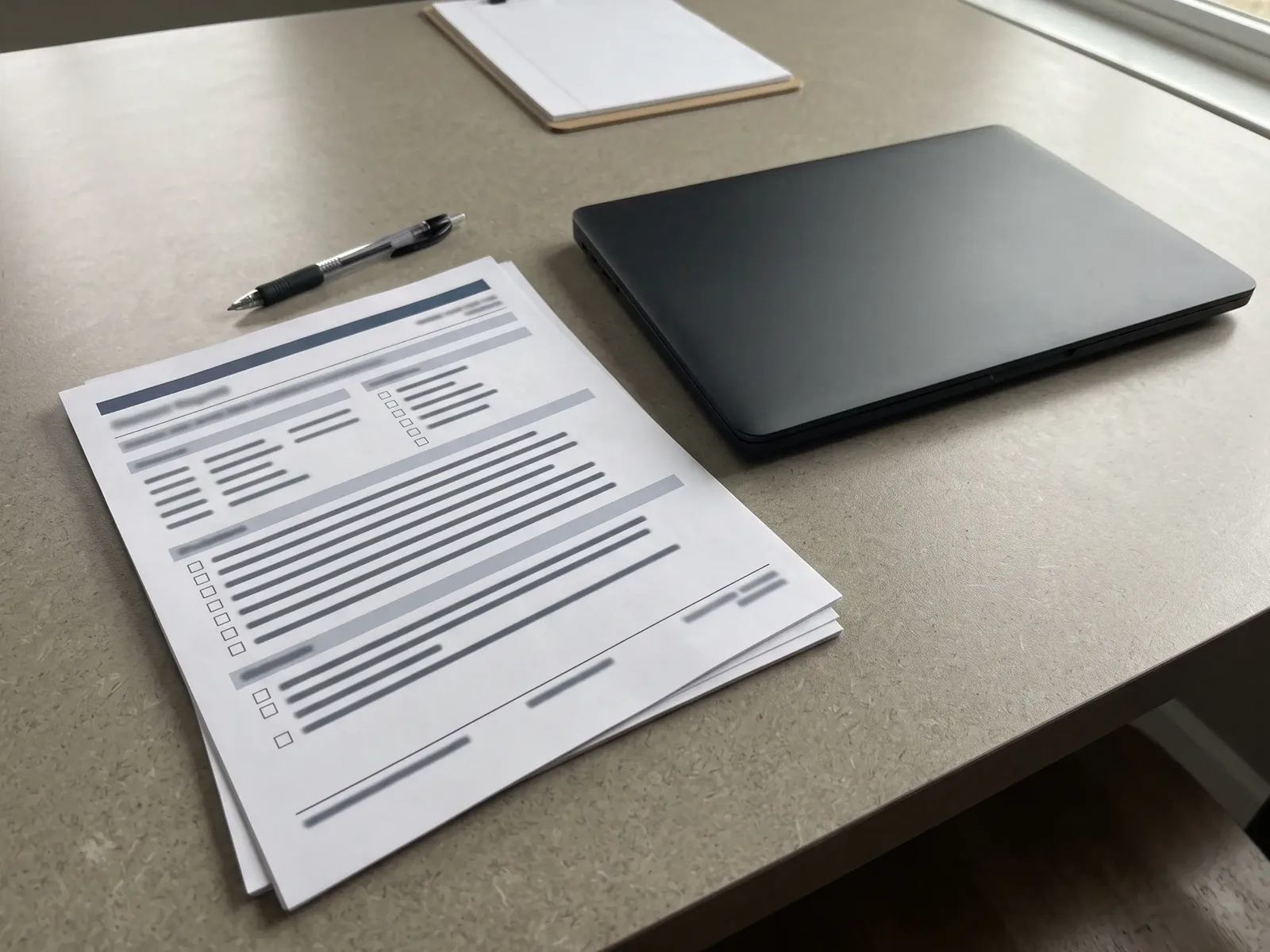 A printed form with blurred text, a pen and a closed laptop on a table