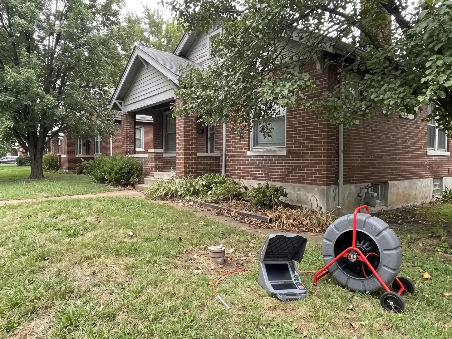 Home exterior with a capped cleanout pipe in the yard, and a sewer camera reel with an open monitor beside it